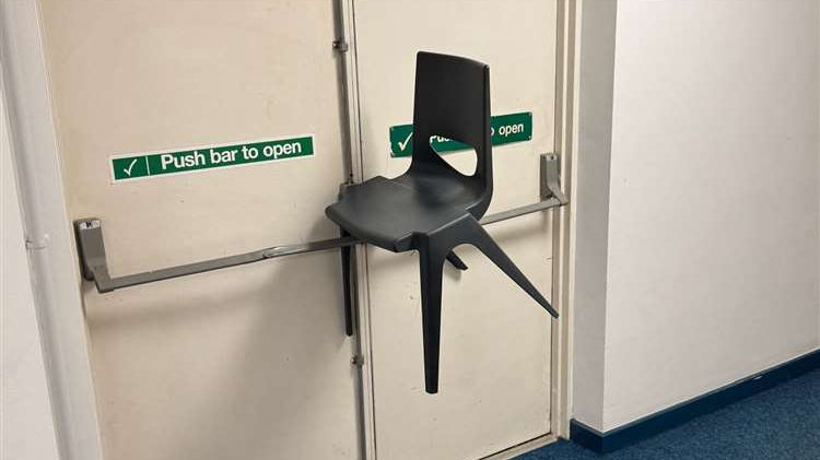 Plastic chair wedged on fire door push bar inside building, obstructing emergency exit
