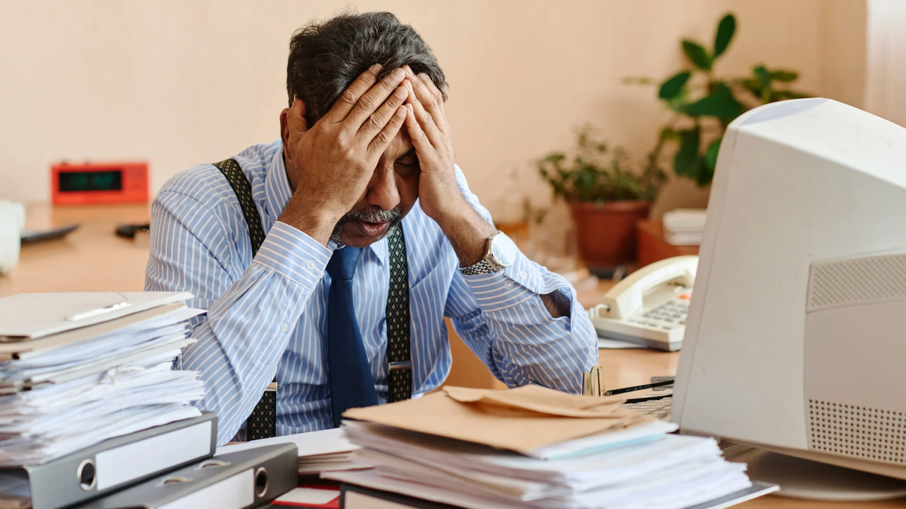Stressed office worker with head in hands at cluttered desk with documents and computer