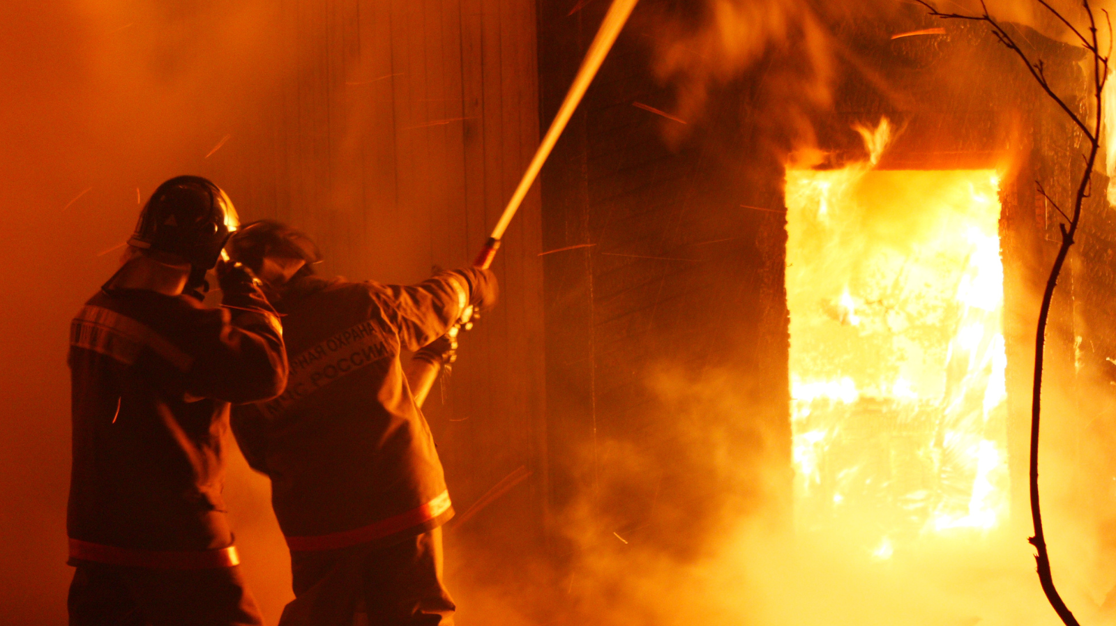 Firefighters extinguishing an intense house fire through a doorway, fire protection concept