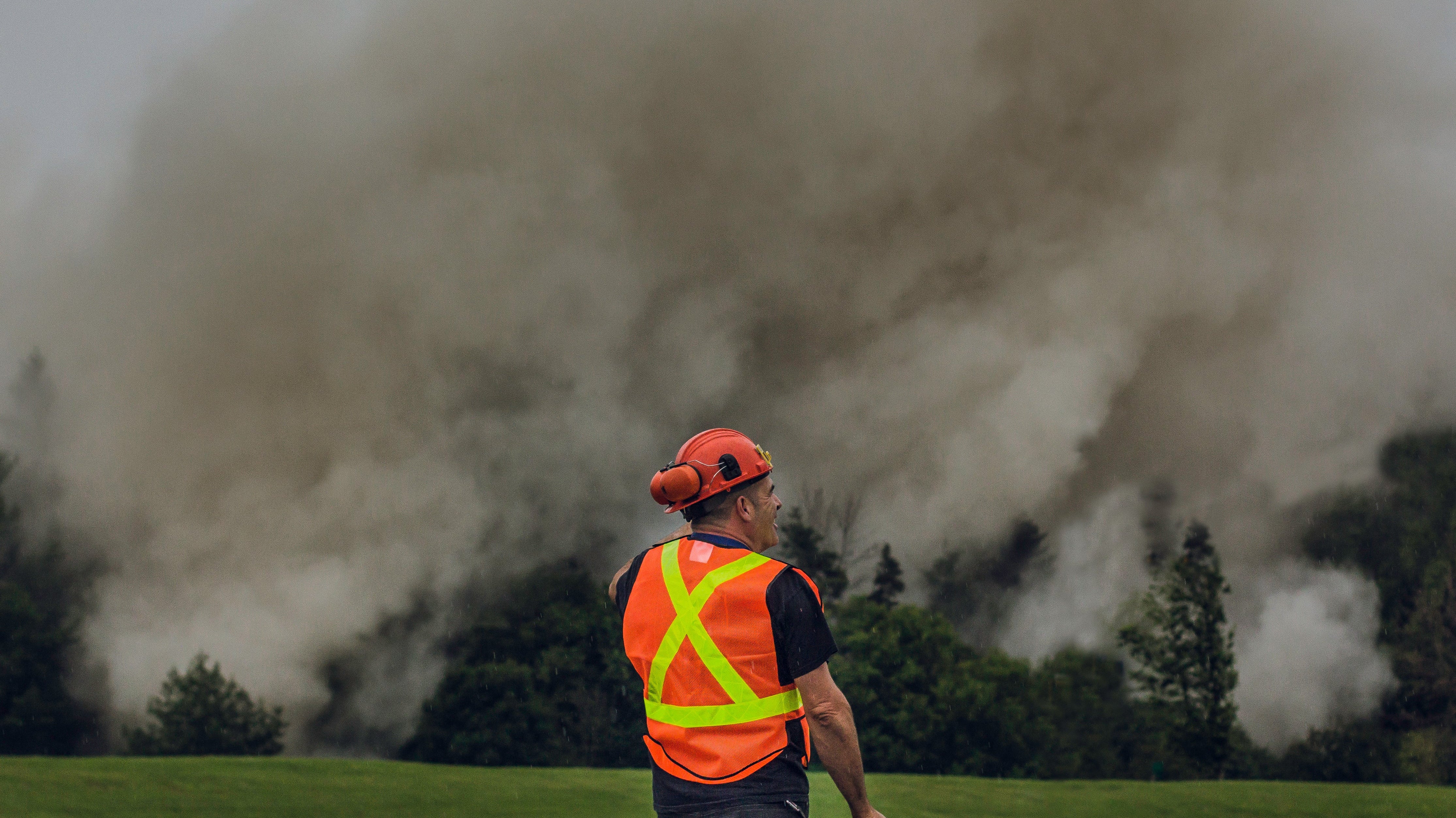Construction worker in safety vest and helmet stands near heavy smoke outdoors