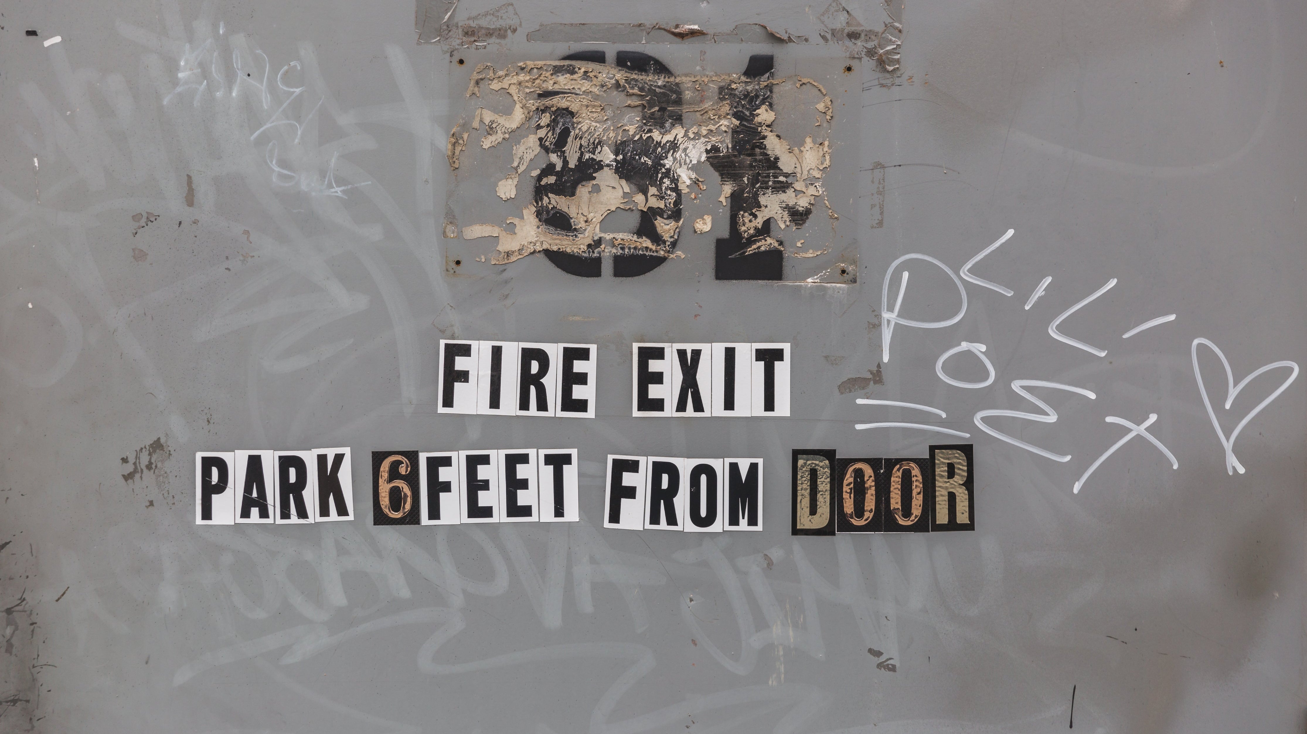 Fire exit sign on gray fire door with graffiti, text reads park 6 feet from door
