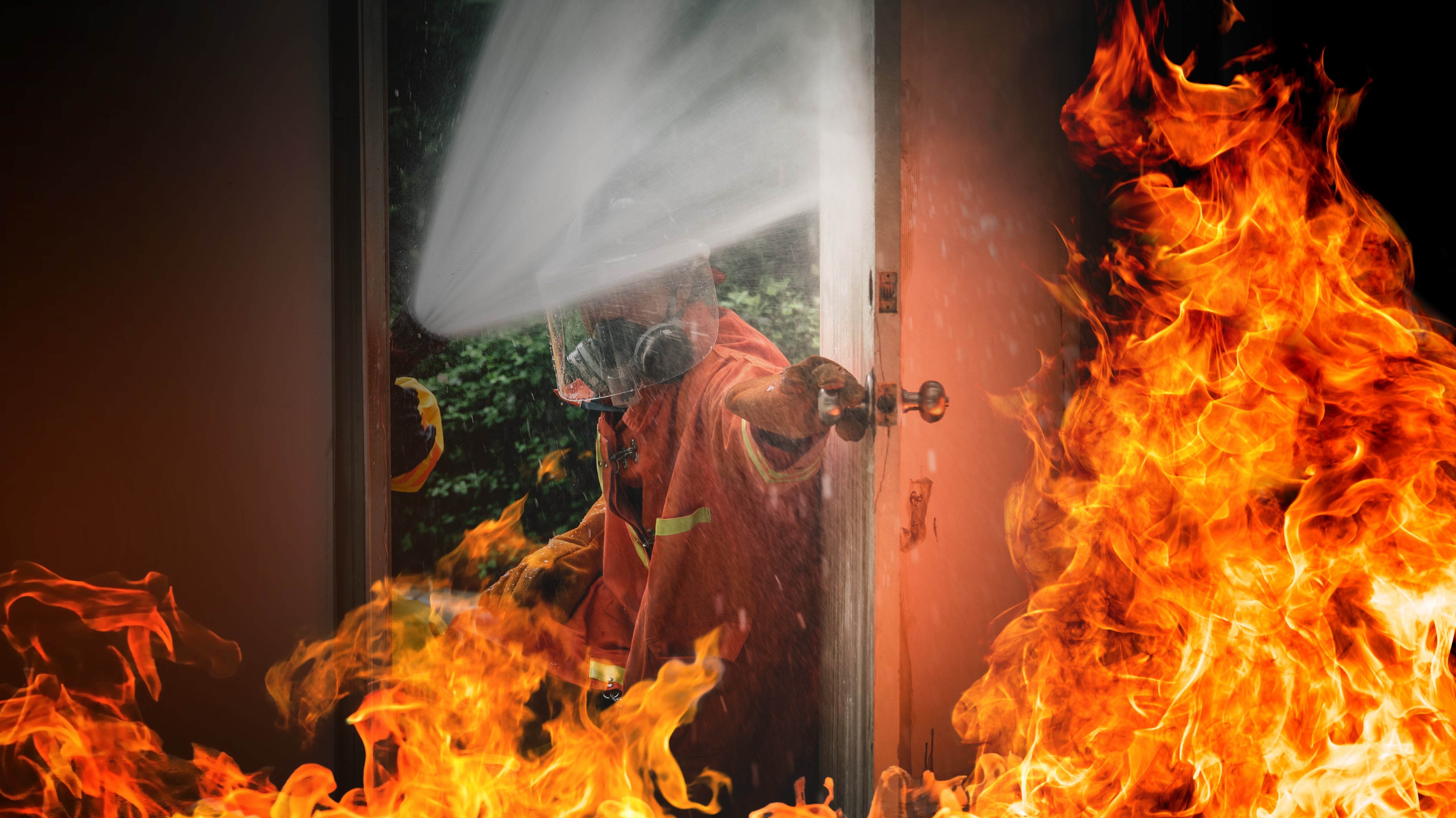 Firefighter spraying water through a fire-resistant door with flames on both sides