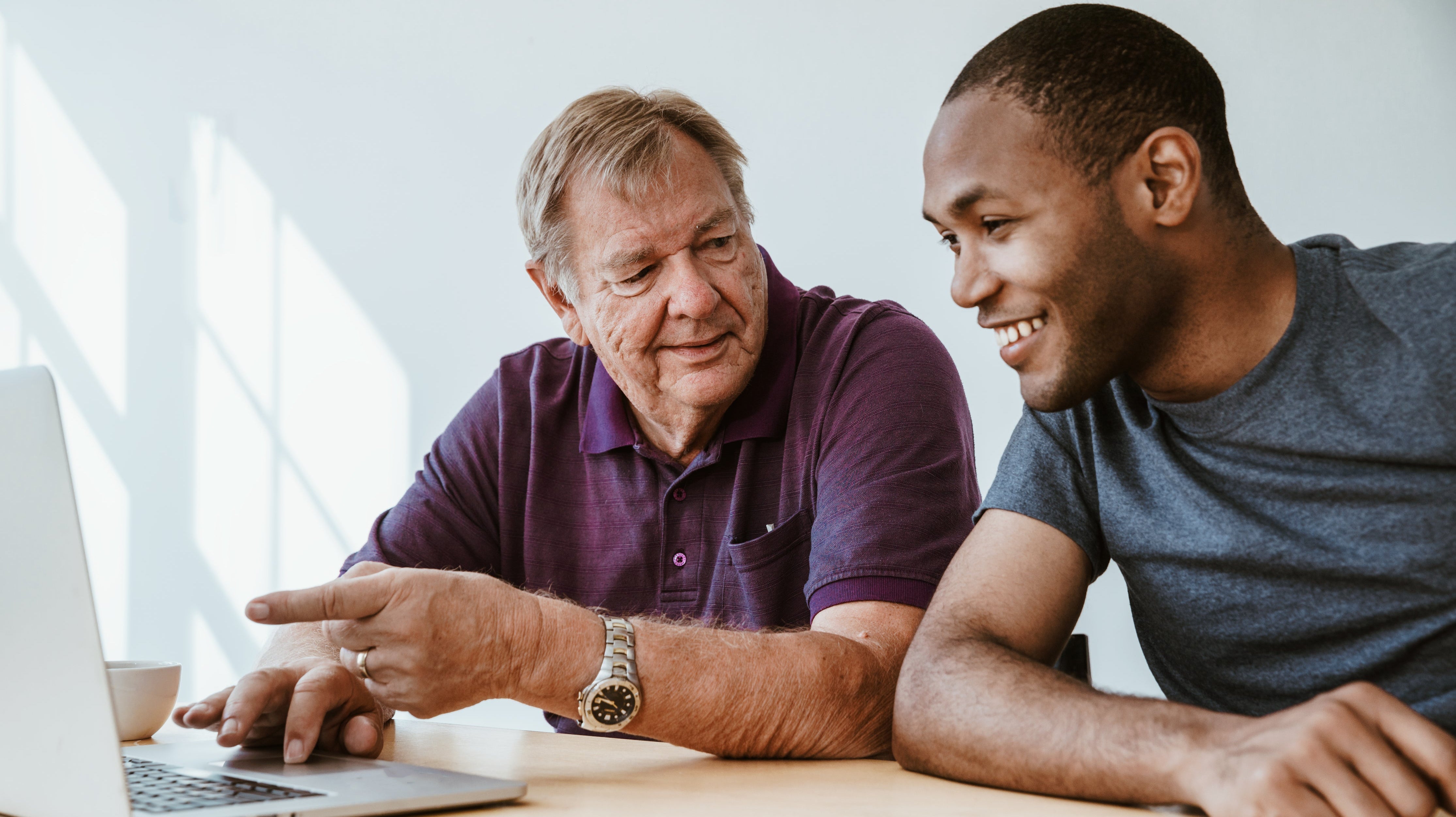 Older man teaching young man at laptop in bright room, learning and mentorship concept