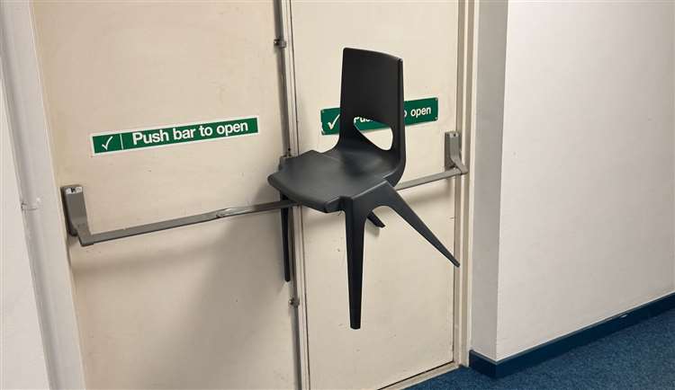 Plastic chair wedged on fire door push bar inside building, obstructing emergency exit
