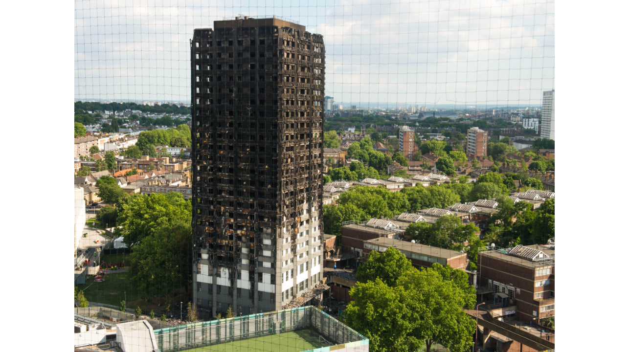 High-rise residential tower with extensive fire damage in urban setting, surrounded by greenery.