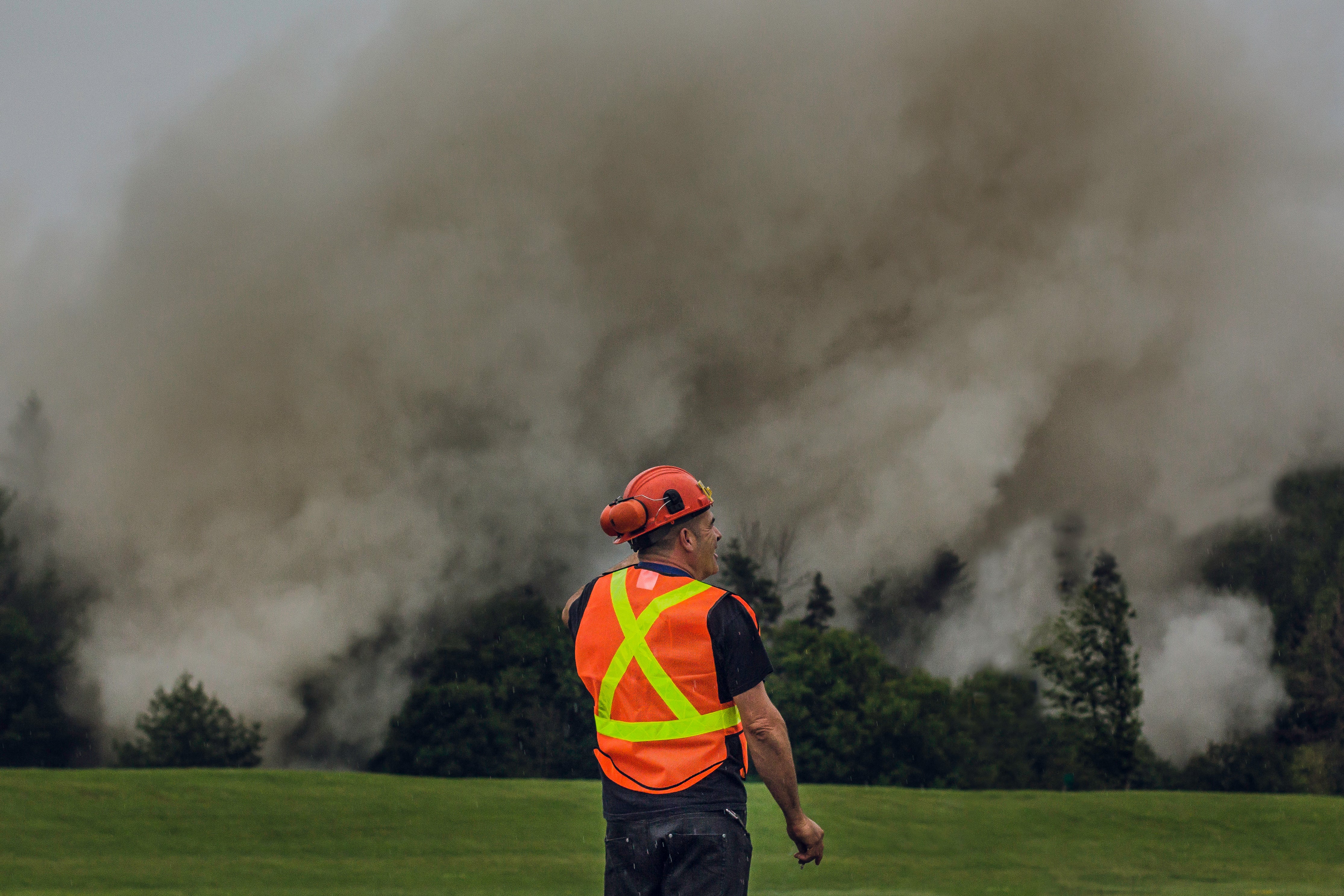 Construction worker in safety vest and helmet stands near heavy smoke outdoors