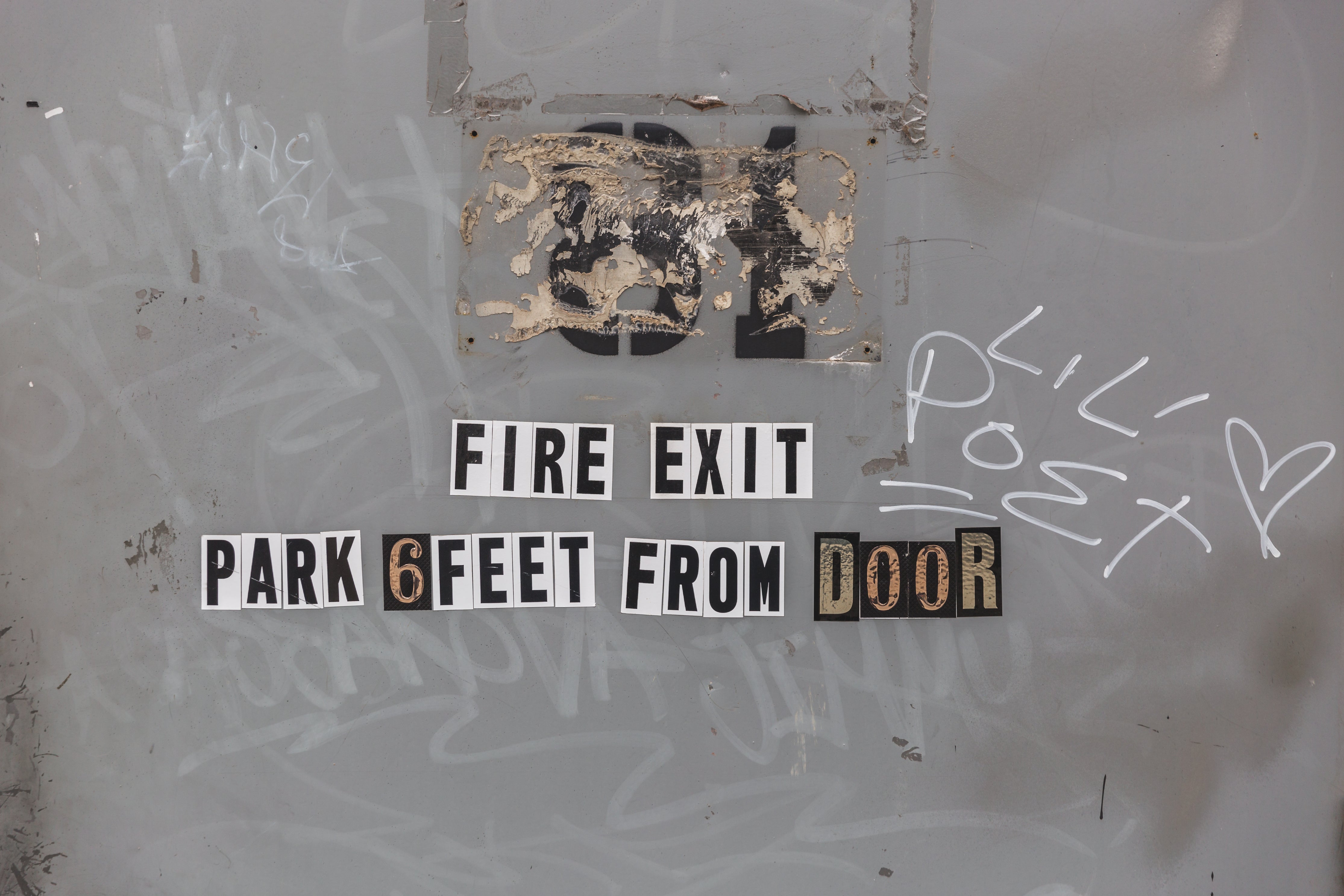 Fire exit sign on gray fire door with graffiti, text reads park 6 feet from door