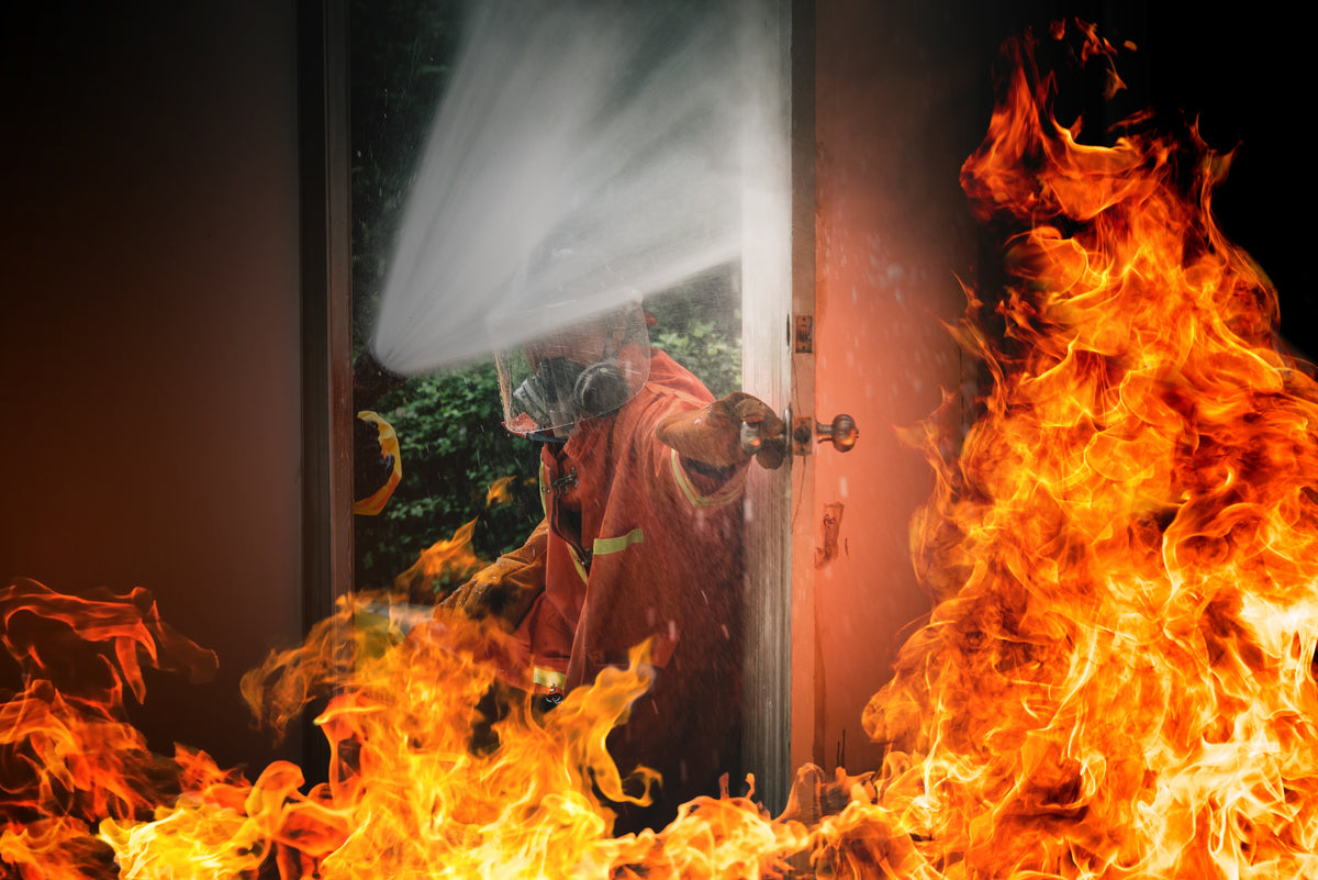 Firefighter spraying water through a fire-resistant door with flames on both sides