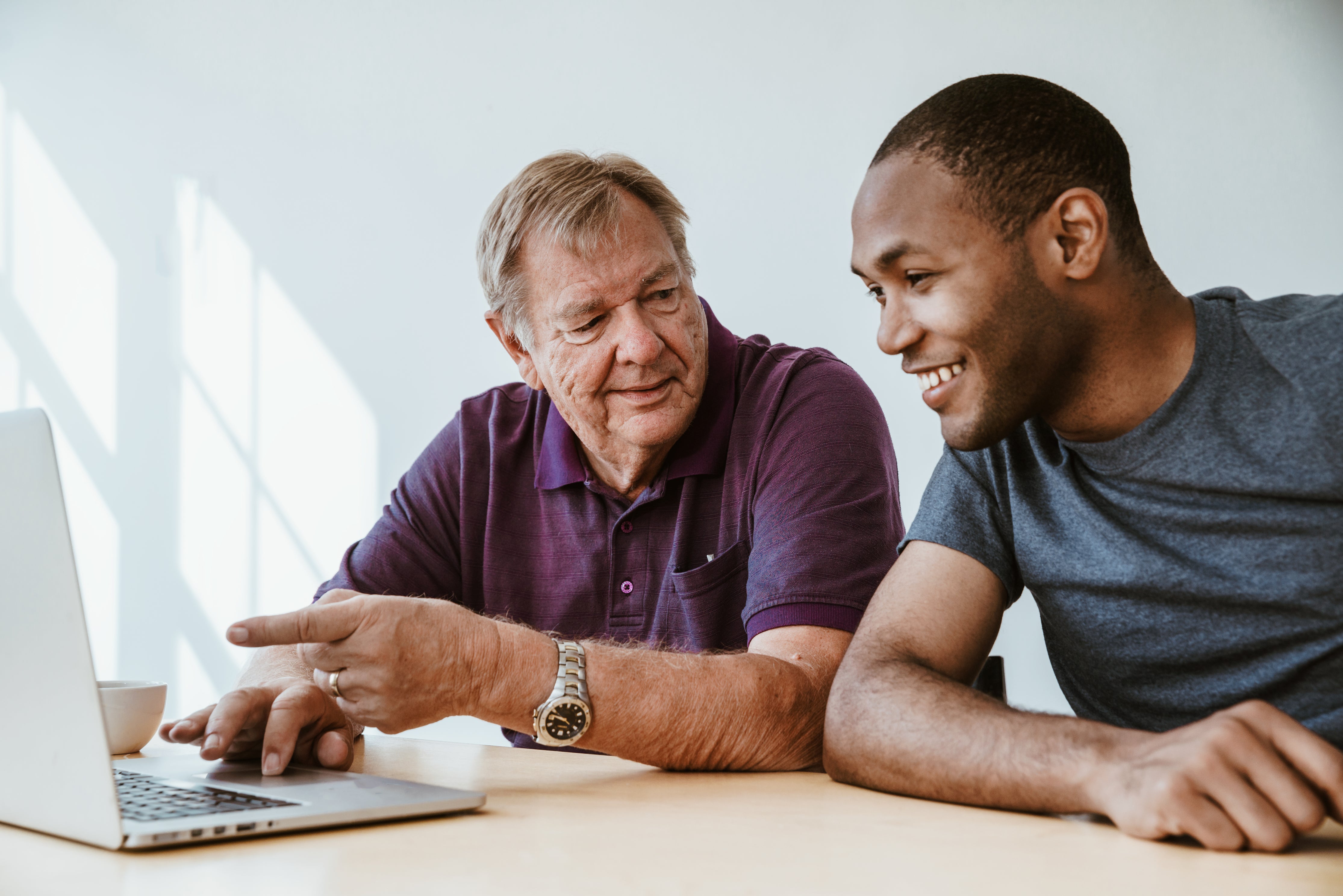 Older man teaching young man at laptop in bright room, learning and mentorship concept