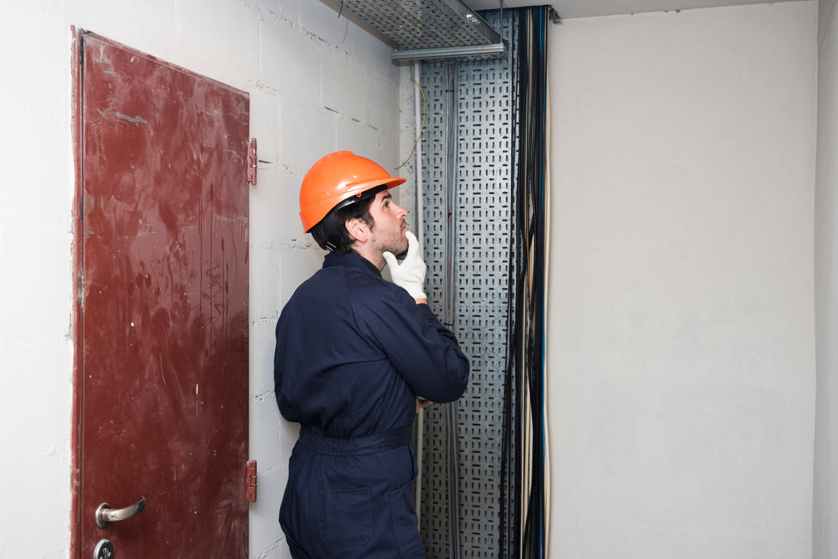 Electrician in orange hard hat inspecting fire door and wiring in industrial setting